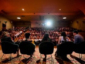 Five people sitting in green velvet chairs in front of a full cinema audience