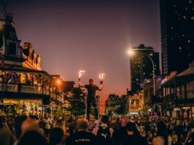 An Adelaide Fringe performer holds fire sticks, standing on a ladder above a crowded Rundle Street.