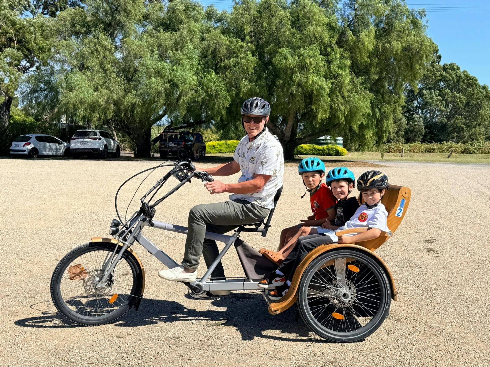 A man riding a TukTuk with 3 children in the seat behind at Hugo Wines