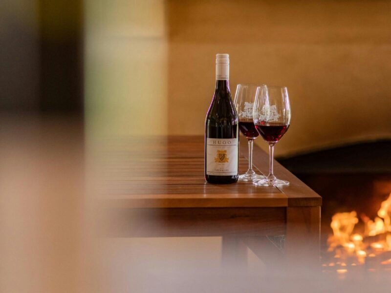 A bottle of red wine and 2 wine glasses with a fireplace in the background