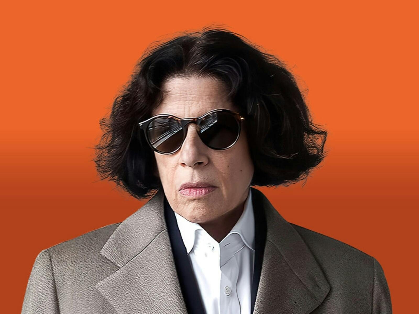 Fran Lebowitz with short, dark hair and sunglasses wearing a tan coat and a white shirt