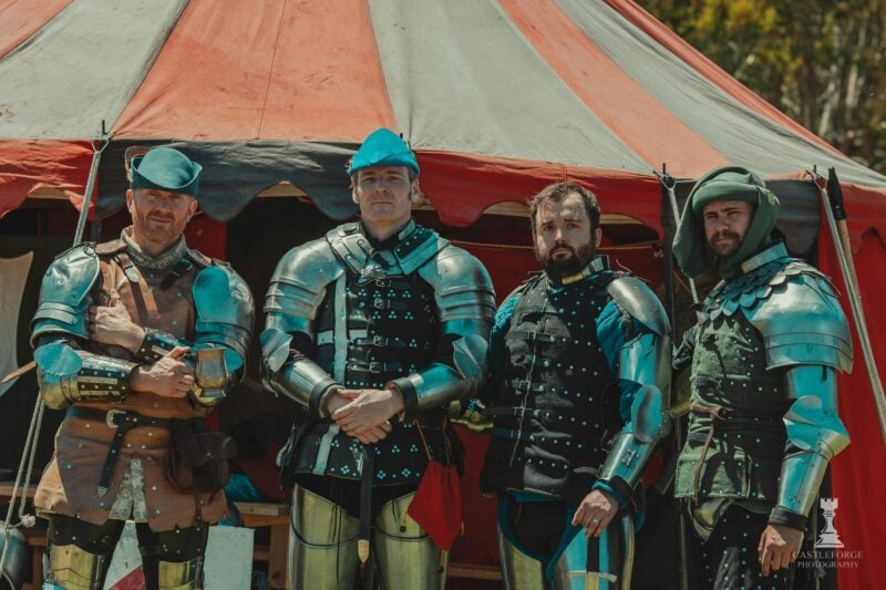 four people dressed as medieval knights in front of a red and white medieval tent