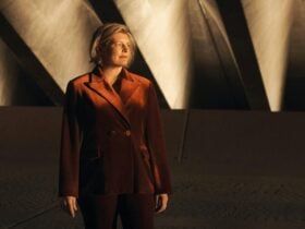 A person stands in a rich orange suit againsta a gabckdrop of natural light and architectural lines