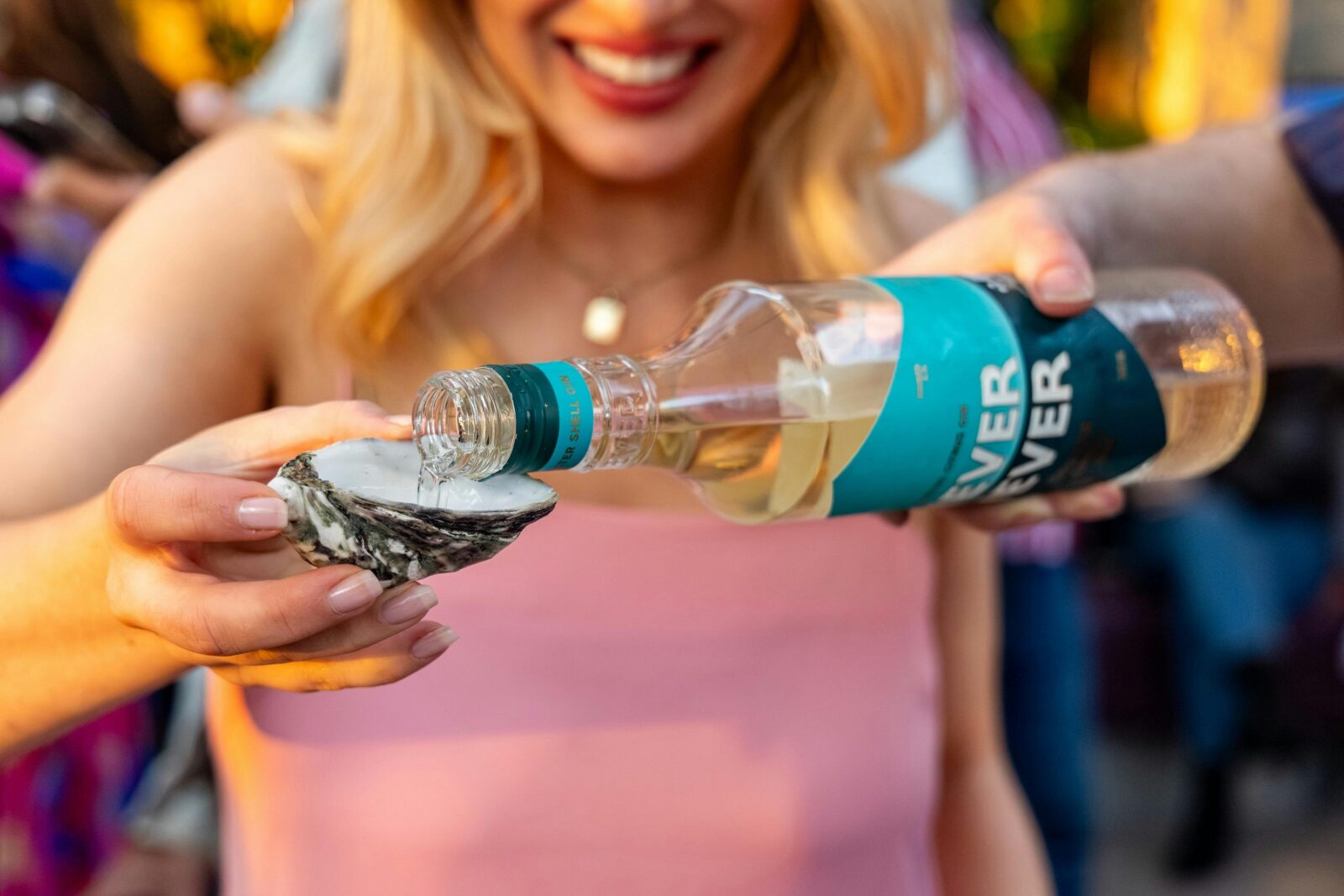 Gin poured into an oyster shell held by a smiling guest.