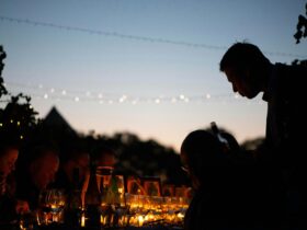 Nighttime photo of stevo pouring wine for guest on long table
