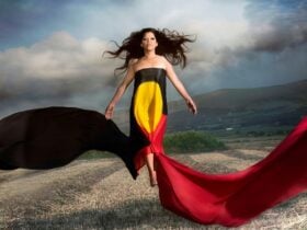 A woman wrapped in an Aboriginal Flag floats above the ground with her hair and arms outstretched