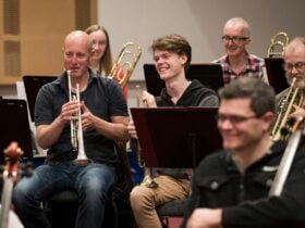 A young person smiling and sitting next to an Orchestra trumpet player, who is also smiling.