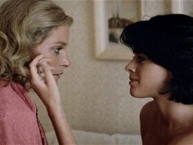 Two women gaze longingly at each other, one runs her hand across the other's cheek.