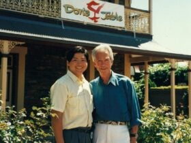 Two smiling people standing together in front of a building with a sign reading ‘Don’s Table’.