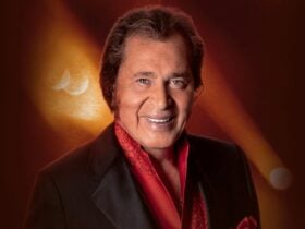 Engelbert Humperdinck smiles warmly, wearing a black tuxedo jacket over a vibrant red shirt
