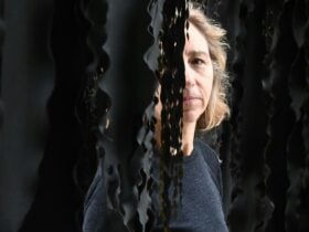 A female artist with blonde hair peering through a black hanging installation