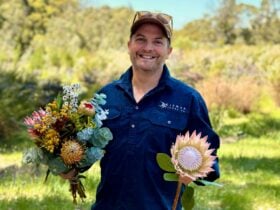 Man standing in farm setting holding flowers in each hand.