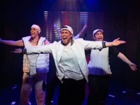 3 performers with outstretched arms, singing in a humorous manner