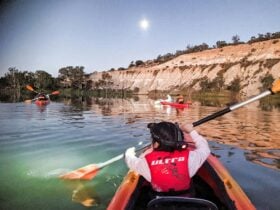 Child in front of double kayak, holding paddle, moves towards full moon and line of cliffs