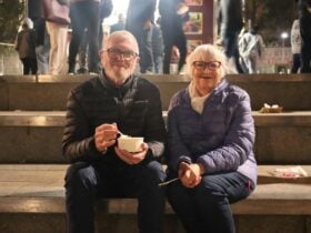 Elderly couple sitting on steps at night, smiling and enjoying food in bowls during the festival.