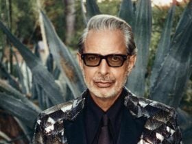 Jeff Goldblum wearing black glasses and a metallic blazer, behind is large, pointed agave plants