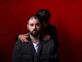 A woman dressed in leather and wearing glasses puts her hands around the neck of a worried young man