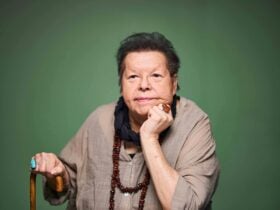 An Elder woman looks slightly off camera with one hand resting on her chin and the other on a cane