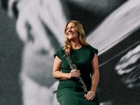 An oboe player in a dark green dress, smiling, holding her instrument
