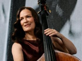 A photo of a double bass player holding their instrument and smiling