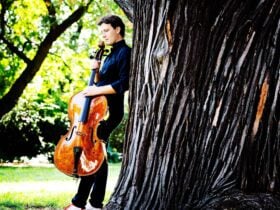 Maximilian Hornung standing against a large tree, holding his cello.