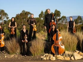 Members of Momentum Ensemble standing in long grass against gum trees and a blue sky.