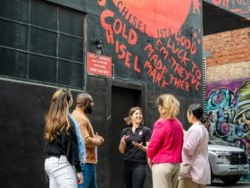 A tour group watches their guide and the street art piece behind them.