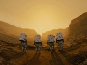 Four astronauts standing together on a rocky, Mars-like landscape at sunset.