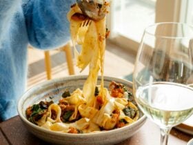Pasta being taken off a main dish to a share plate with glass of wine