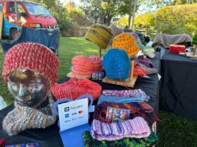 A stall displaying colourful woollen hats and warm scarves. Set against a black background.