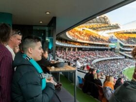 Man standing in room facing a crowd and oval holding a beer