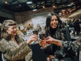 Two women enjoying a glass of red wine in a lively, night market atmosphere