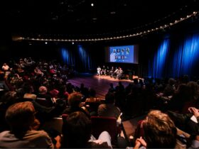 A diverse crowd is seated, listening intently to a panel discussion taking place on stage.