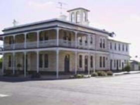 A magnificent two storey, stone building with a return verandah with white posts and lacework,