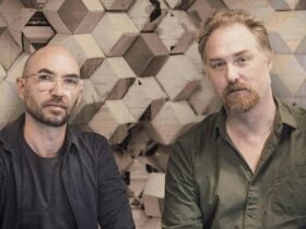 One man has a shaved head and wears a blue shirt, the other has light hair and wears a green shirt.