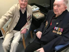 Two elderly gentlemen sitting with their war campaign medals on their left side..