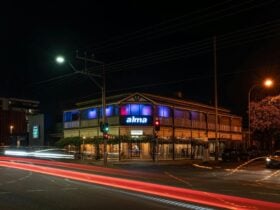 Night view of a two-story building with Alma signage, red-lit windows and a traditional verandah.