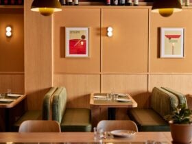 a room clad with pale wood, and light green booths, featuring vibrant red pieces of art on the walls