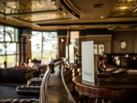This photo shows a wooden table, a menu, large beach side windows , leather couches in Horizons.