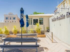 The paved beer garden of a country pub featuring picnic tables, closed umbrellas and plants.