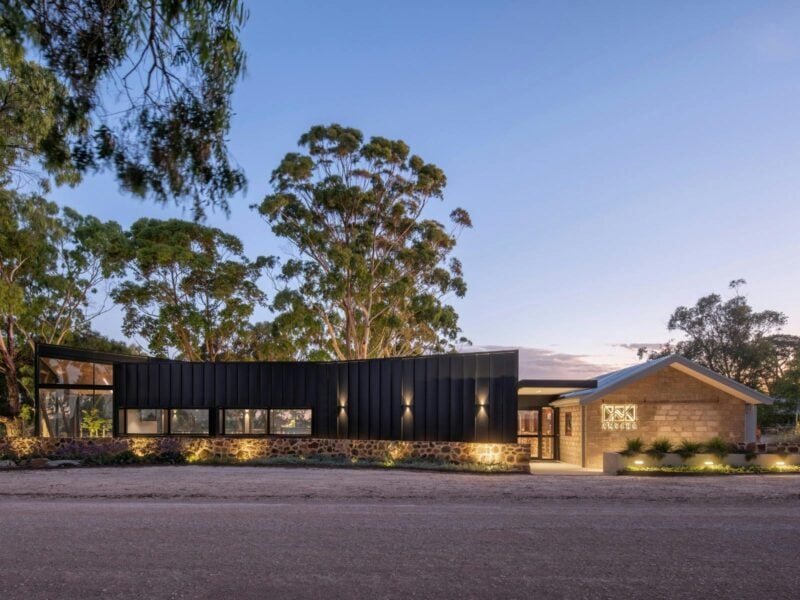 The sun sets over a modern building under towering gums