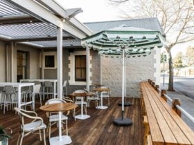 The outdoor deck of a country pub, featuring a striped umbrella and bistro-style seating.