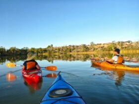 on a mirror-flat river, 2 kayakers paddle past cliffs in the evening golden light