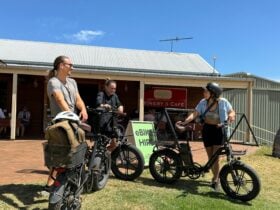 Three young adults laughing as they lean on their eBikes outside Oxenberry Farm Cellar Door