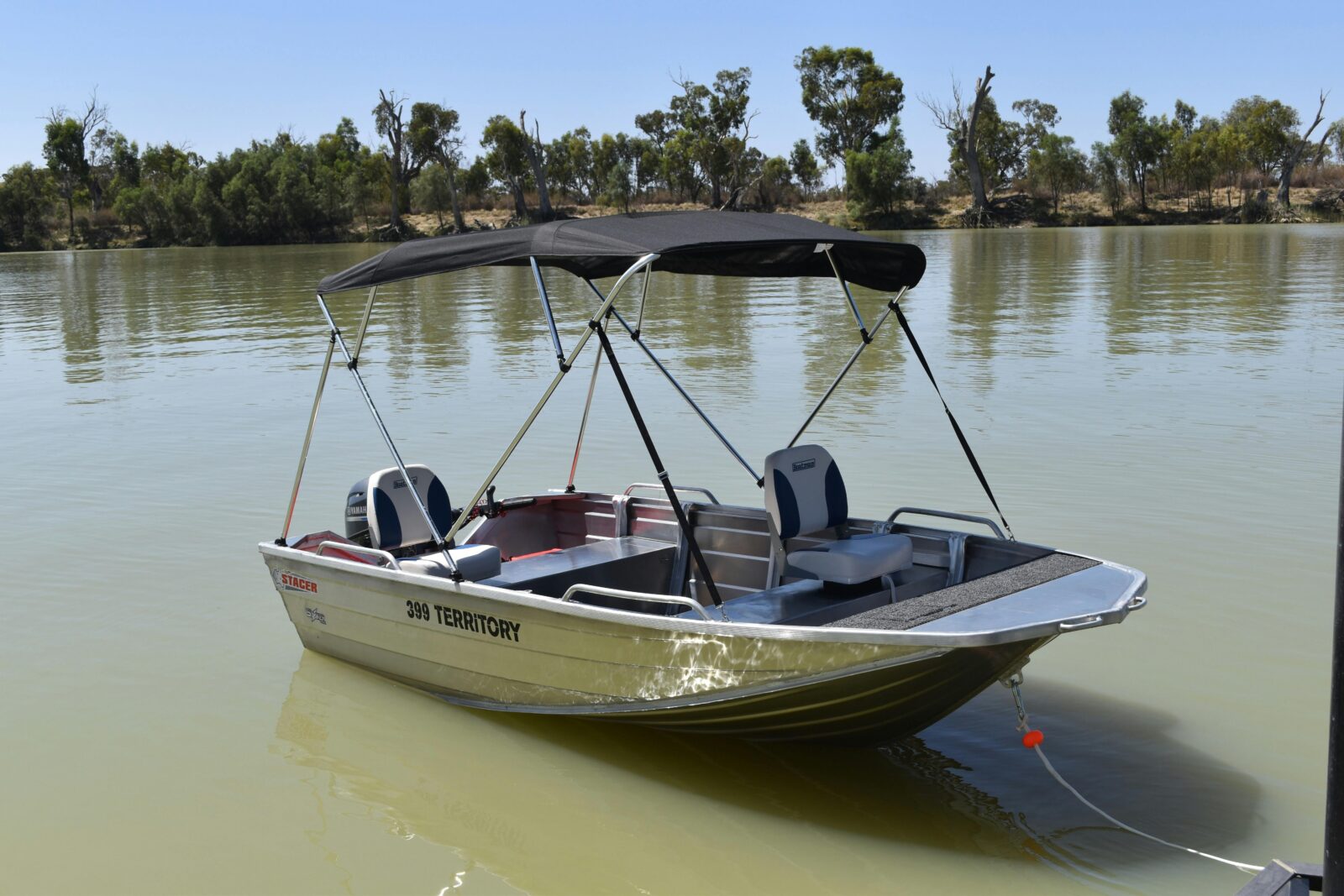 Small tinny hire boat with black canopy on the River at Waikerie, surrounded by calm water & trees