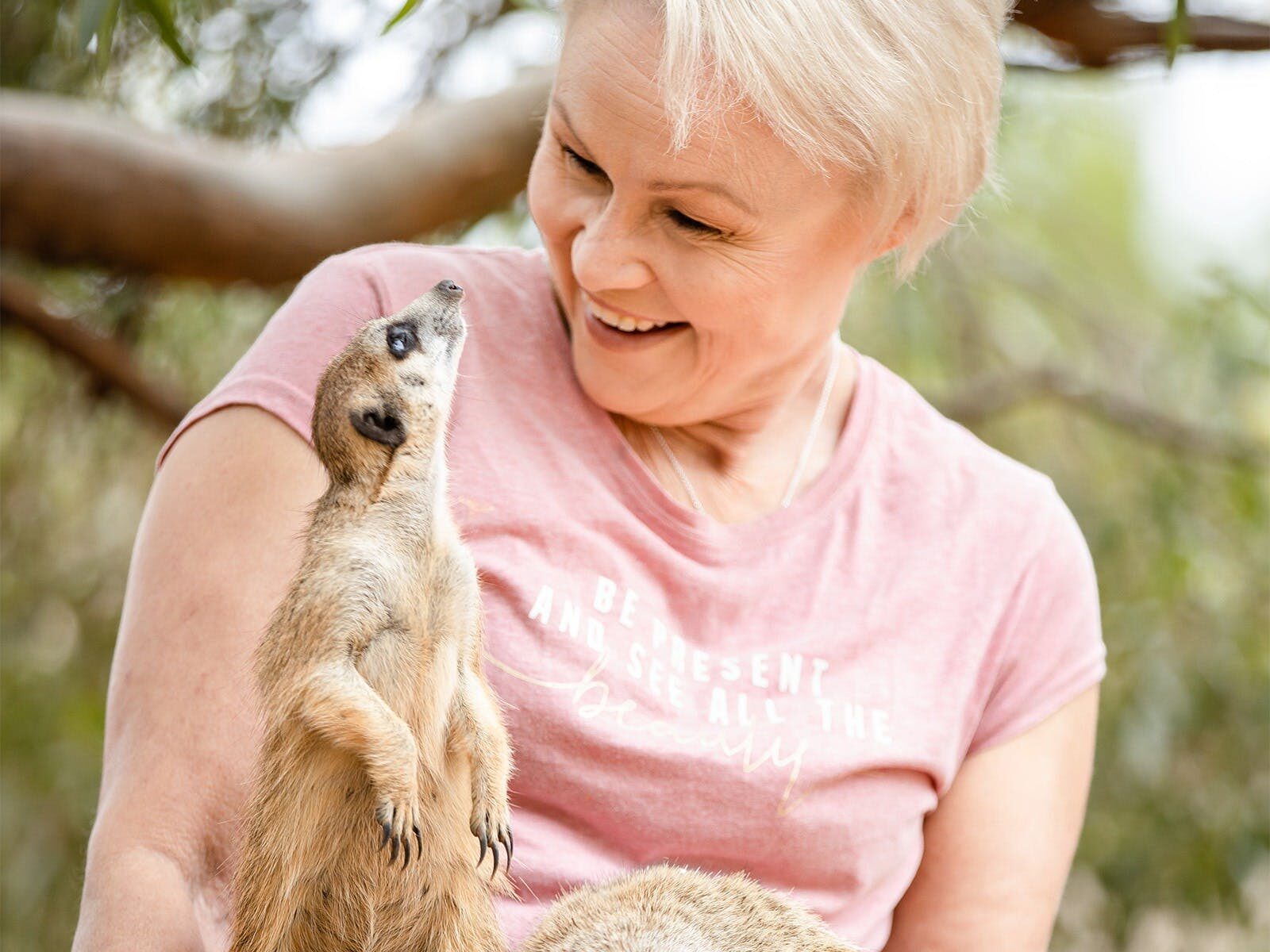 Woman smiling excitedly as Meerkat looks up at her from lap