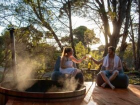Couple share a drink by the hot tub as the sun sets through the pine trees