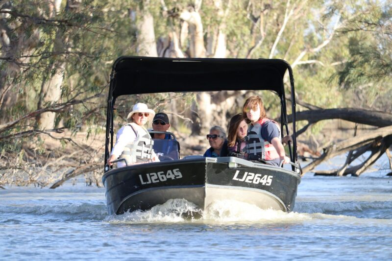 a small boat with four passengers navigating a creek surrounded by fallen trees in the Riverland