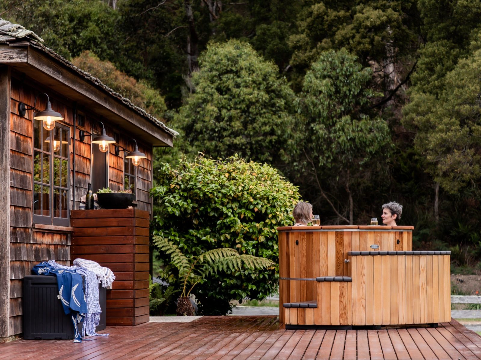 Photograph of a hot tub, with two women sitting in it. The hot tub sits on a wooden deck