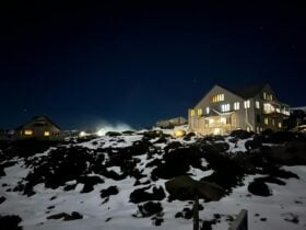 A three story ski lodge at night, with lights in the windows, a clear night sky, snow on the ground